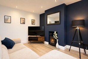A modern living room with a sofa, a flat-screen TV, a fireplace, and a floor lamp.