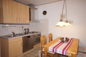 A kitchen with wooden cabinets, a stainless steel stove, a sink, and a dining table with chairs. - Holiday apartment Greetsiel (Osteel)