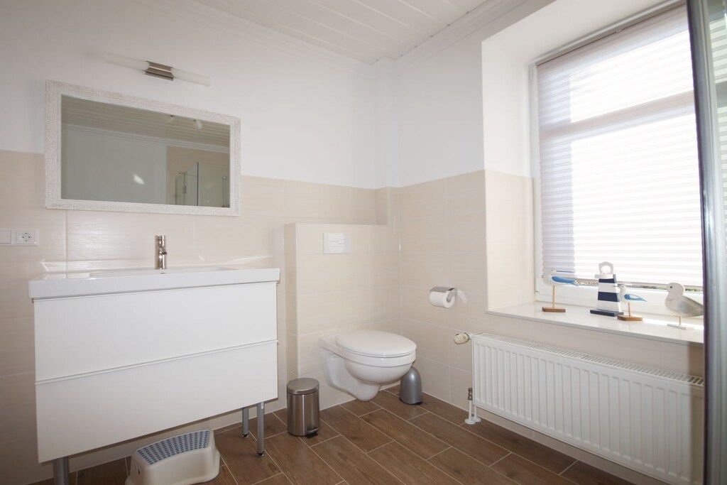 Ein Badezimmer mit weißem Waschbecken, Spiegel, Toilette und einem Fenster mit Jalousien.