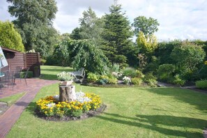 A well-maintained garden with a wooden deck, a variety of plants, and a tree stump centerpiece. - Holiday apartment Greetsiel (Osteel)