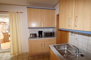 A kitchen with wooden cabinets, a stainless steel sink, and a microwave. - Holiday apartment Greetsiel (Osteel)