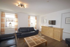 Een woonkamer met een zwarte leren bank, een houten salontafel, een televisie op een houten kast en een plafondventilator.