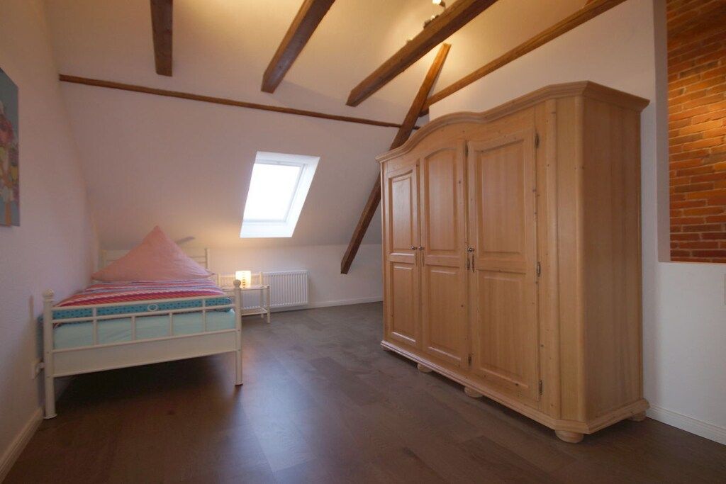 A bedroom with a bed, a wardrobe, a radiator, and a sloped ceiling with exposed beams.