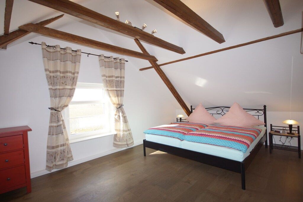 Un dormitorio con techo inclinado, una cama con almohadas rosas, un aparador rojo y una mesita de noche con una lámpara.
