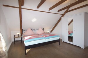 Ein Schlafzimmer mit schrägen Wänden, einem Bett mit gemustertem Überwurf, einem Nachttisch mit Lampe und einem Kleiderschrank.