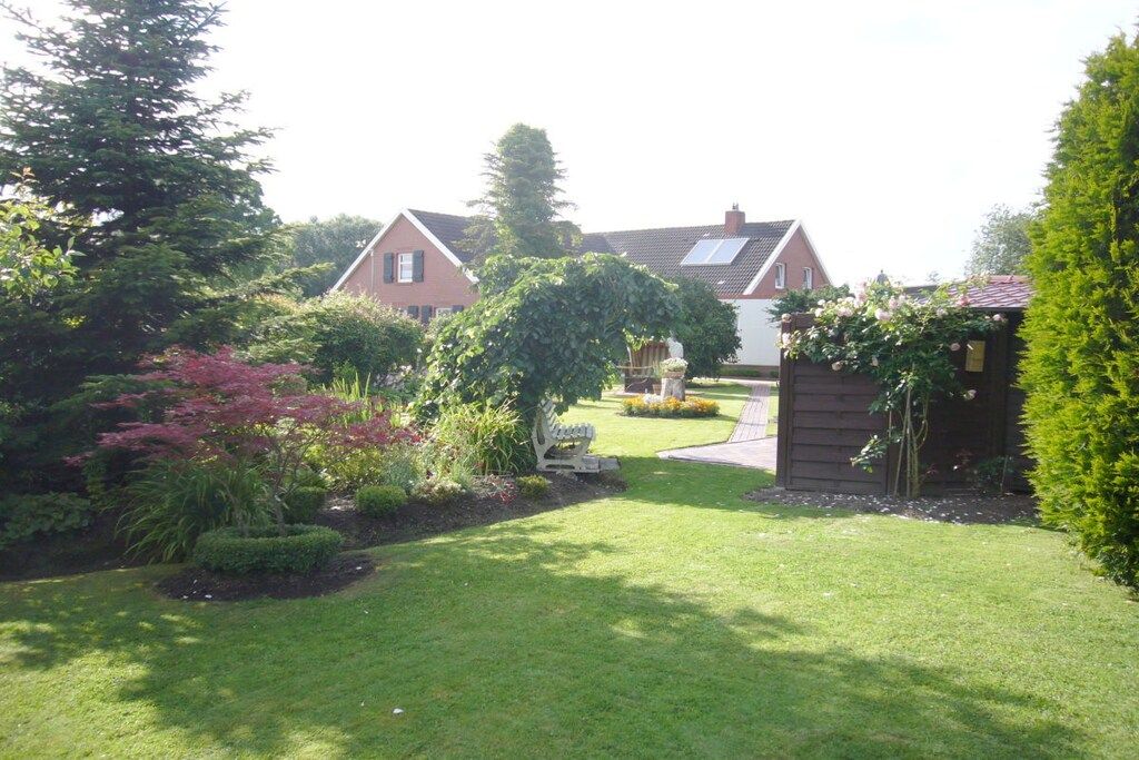 A residential property with a well-maintained lawn, a wooden fence, and a variety of shrubs and trees.