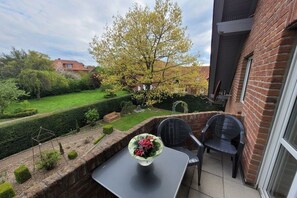 Eine Terrasse mit Tisch und zwei Stühlen, ein Garten mit Hecke und eine Ziegelmauer.