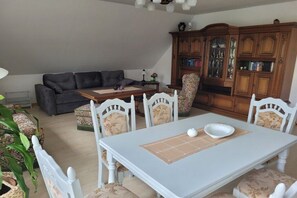 Un coin repas avec une table et des chaises blanches, un canapé et un meuble en bois doté de portes en verre.