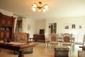Un salon traditionnel avec une table basse en bois, des fauteuils à motifs floraux, une table à manger avec des chaises et un lustre.