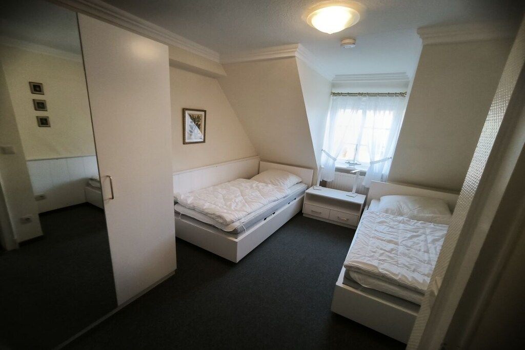 A bedroom with two beds, a bedside table, a nightstand, a mirror, and a window with curtains.
