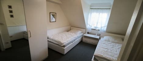 Un dormitorio con dos camas, una mesita de noche, un espejo y una ventana con cortinas.