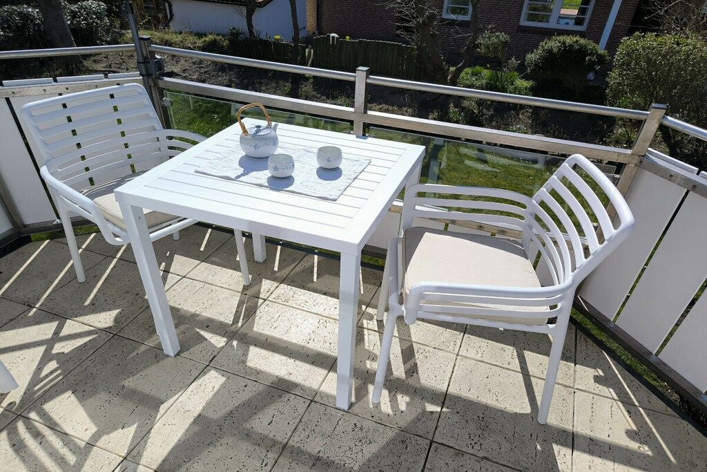 A white table and chairs on a balcony with a view of a garden and a building in the background.