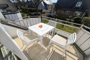 Ein Balkon mit einem weißen Tisch und Stühlen, einer Obstschale und Blick auf Häuser und Grünflächen.