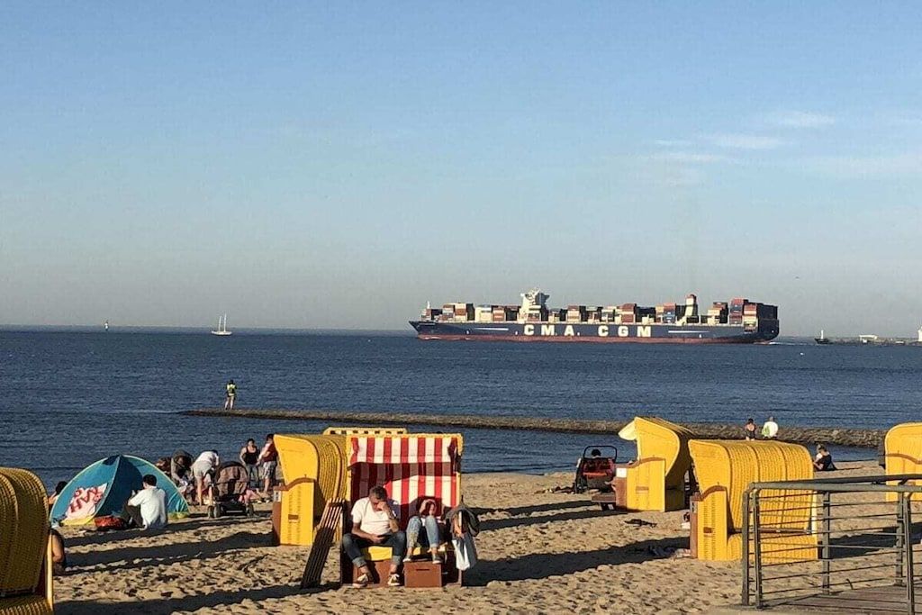 Een strand met gele strandhutten en een grote vrachtschip op de achtergrond.
