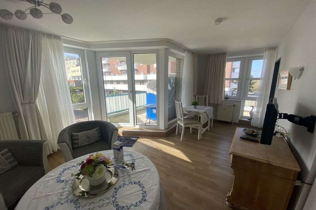 A room with a dining table set for two, a sofa, a TV, and a view of a balcony with a pool.
