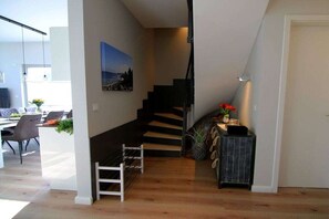 A modern interior with a staircase leading to a second floor, a dining area with chairs and a table, and a small plant on a side table. - Holiday home with 3 bedrooms (Heiligenhafen)