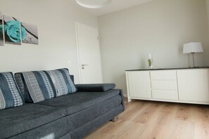 A modern living room with a grey sofa, patterned cushions, a white cabinet, and a door. - Holiday home with 3 bedrooms (Heiligenhafen)