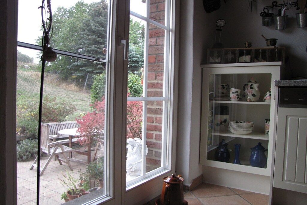 Eine Küche mit einem großen Fenster, einem Holztisch im Freien und einem Schrank mit Geschirr.