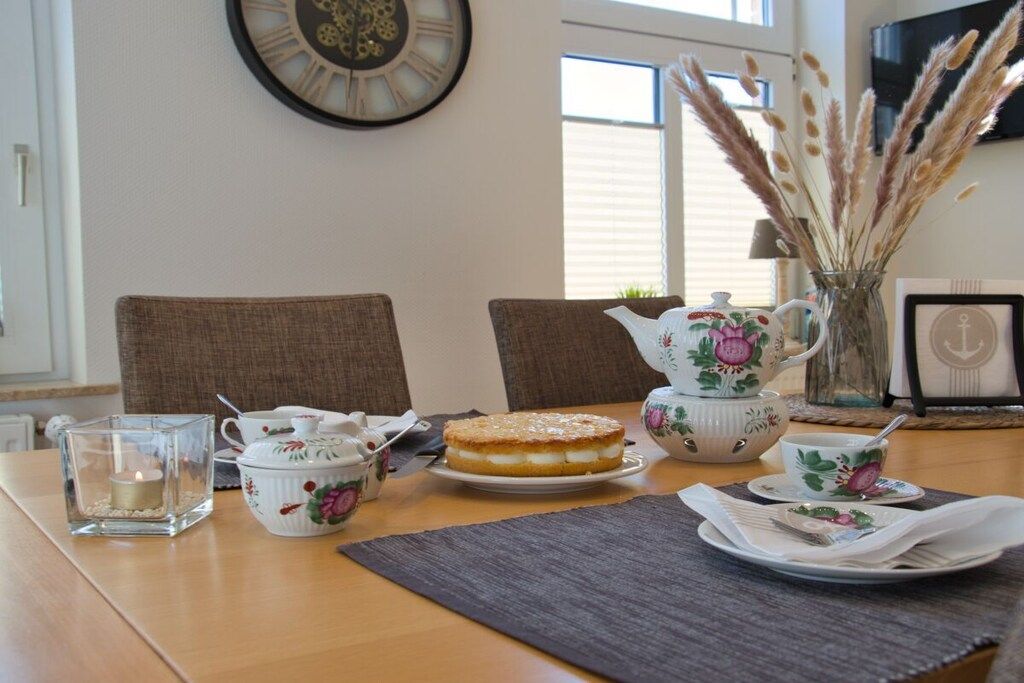 A dining table with a cake, teacups, a teapot, and a candle in a glass holder.