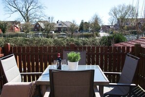 An outdoor patio with a table and chairs, surrounded by a wooden fence, overlooking a residential area. - MS Apartments | Sielterrasse 1 (Ditzum)