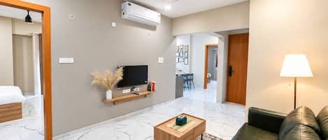 A modern living room with a flat-screen TV, a wooden coffee table, a leather sofa, and a ceiling fan.