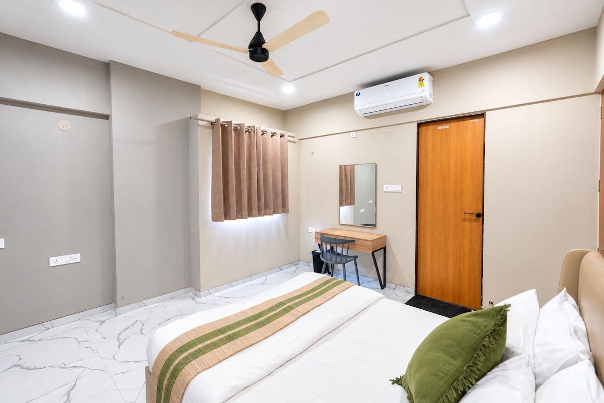 Et hotelværelse med seng, skrivebord, stol, garderobeskab, ventilator og aircondition.