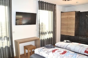 Ein Schlafzimmer mit einem Bett, einem an der Wand befestigten Fernseher, einem Holztisch und einem Kleiderschrank.