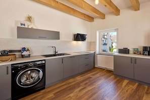 Eine moderne Küche mit integriertem Waschmaschine, grauen Schränken, Holzbalken und einem Fenster mit Blick hinaus.