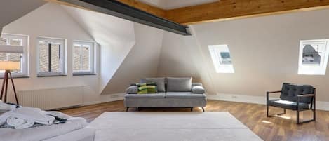 A bedroom with a sloped ceiling, a bed, a sofa, a chair, and a window.