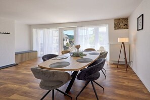 Un comedor con mesa de madera, sillas tapizadas en gris y vistas amplias por ventanas grandes.