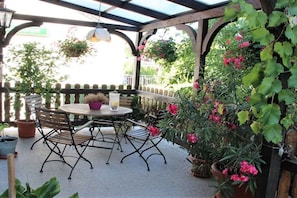 Un patio al aire libre con una mesa redonda y sillas, rodeado de plantas y flores en macetas.