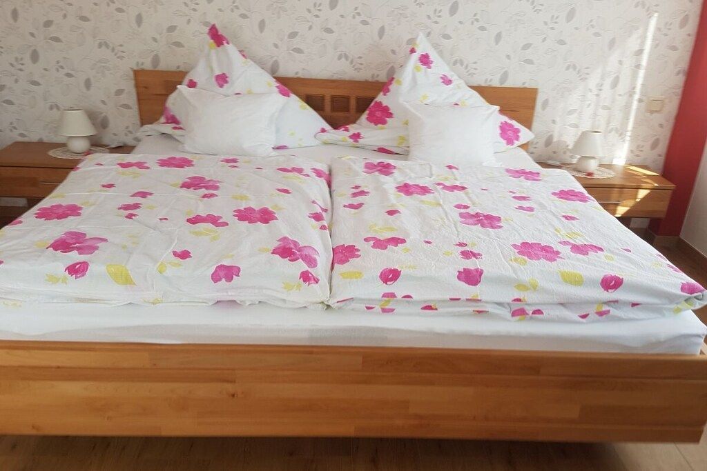 Ein Bett mit einer blumigen Tagesdecke, einem Holzkopfende und zwei Nachttischen mit Lampen.