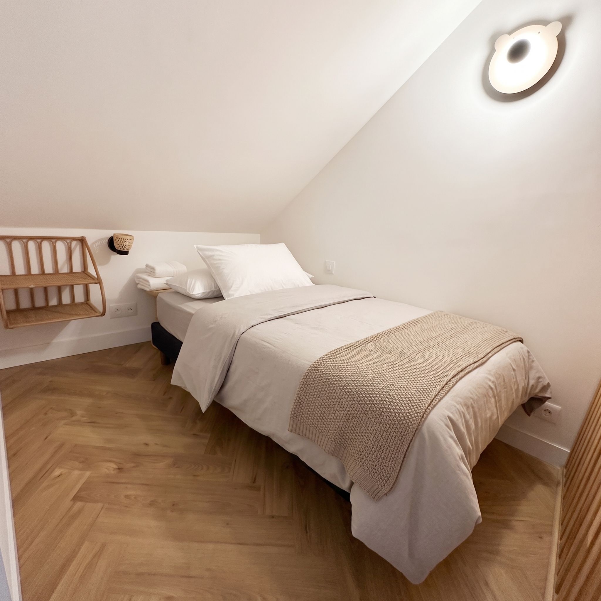 A single bed with a headboard, a bedside table, a wall-mounted light fixture, and a wooden floor.