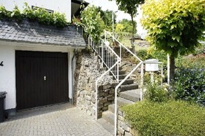A stone staircase leading to a black garage door, surrounded by greenery and a small white utility box. - Holiday apartment with 1 bedroom (Treis-Karden)