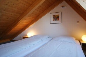 A room with a sloped ceiling, two beds with white bedding, a framed picture on the wall, and bedside lamps. - Holiday apartment with 1 bedroom (Fehmarn)