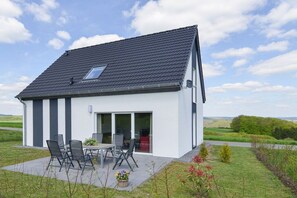 A modern house with a sloped roof, a patio with outdoor furniture, and a view of the countryside. - Holiday apartment with 3 bedrooms (Gillenfeld)