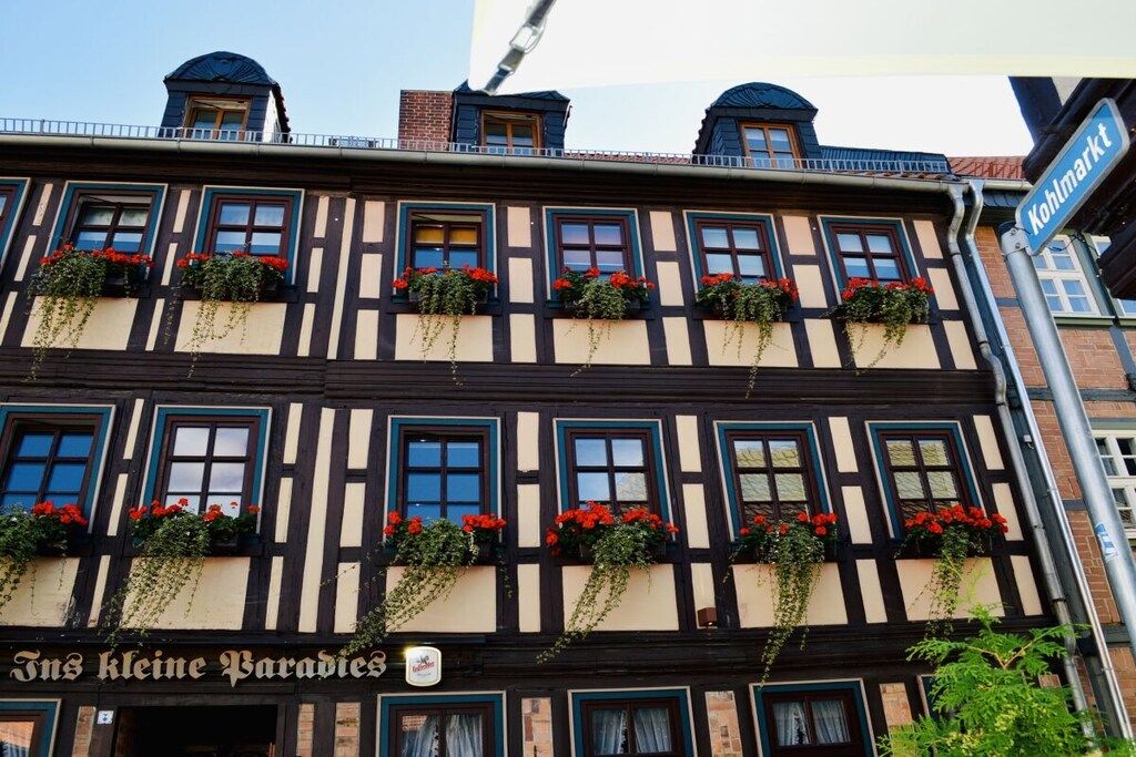 Un edificio tradicional con entramado de madera y múltiples ventanas, algunas con jardineras, y un letrero que dice 'Tns Kleine Paradies'.
