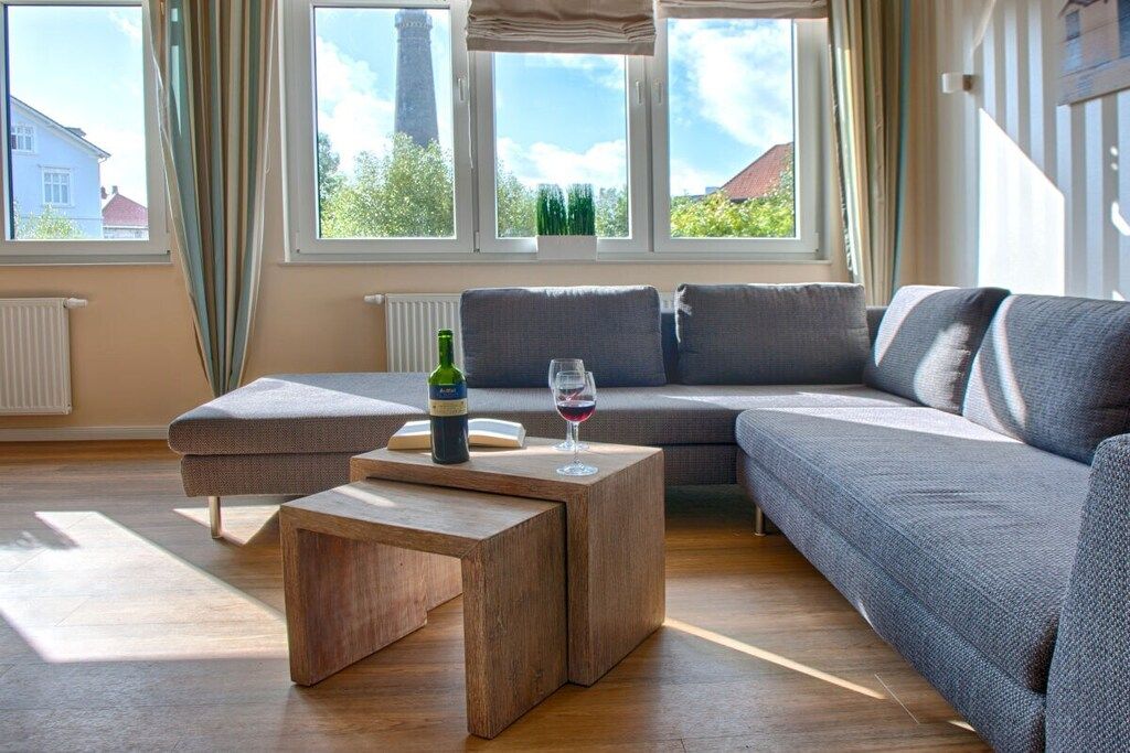 A modern living room with a sectional sofa, a wooden coffee table, and a view of a building through large windows.