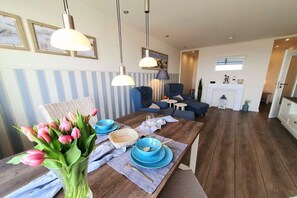 A dining area with a wooden table set for two, blue plates, and a vase of pink tulips. - Holiday apartment with 1 bedroom (Heiligenhafen)