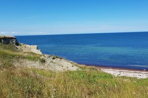 Un paisaje costero con cielo despejado, una playa arenosa y un acantilado cubierto de hierba.