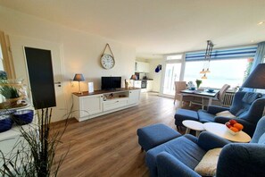 A modern living room with a sofa, a TV, and a dining area with a table and chairs. - Holiday apartment with 1 bedroom (Heiligenhafen)