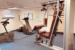 A gym with cardio machines, weight training equipment, and a wall-mounted TV. - Holiday apartment 109 in the Lord Nelson (Cuxhaven)