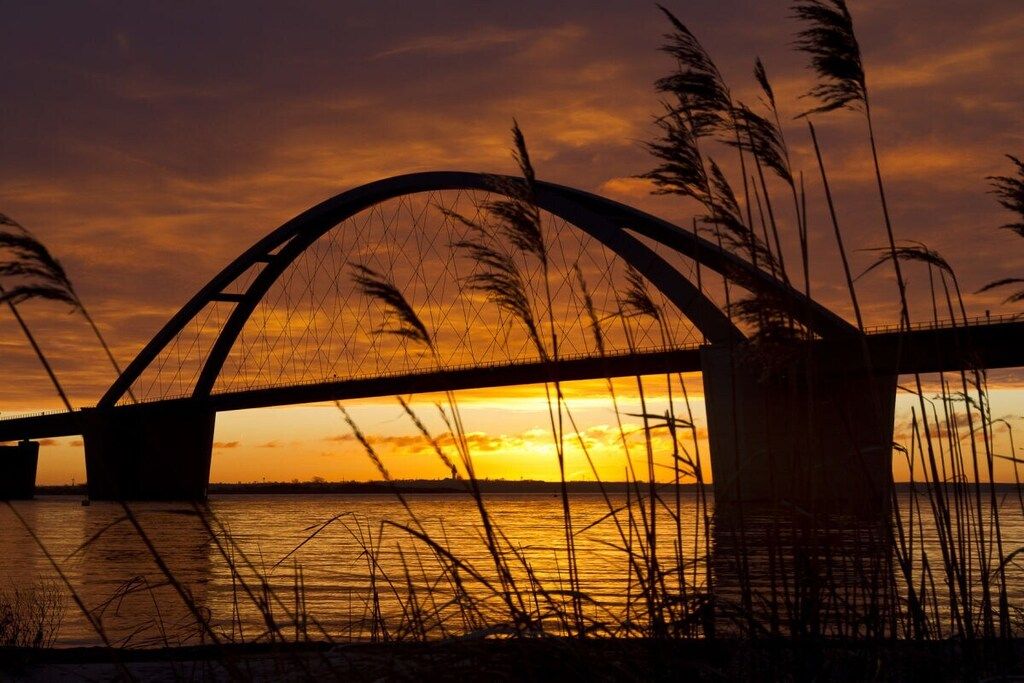 A bridge with a curved arch over a body of water during sunset.