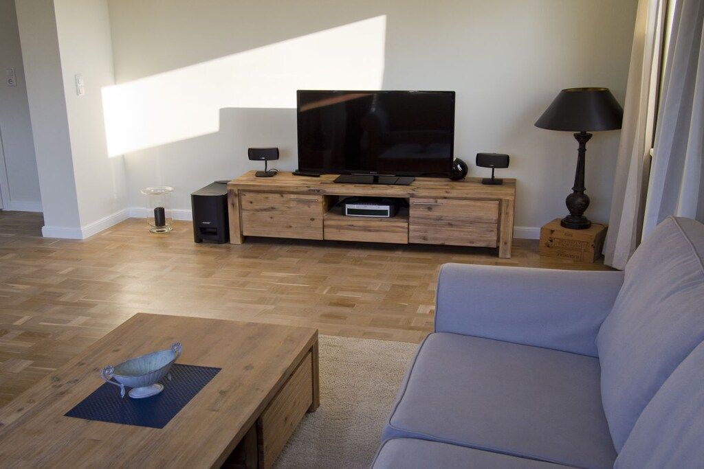 Ein modernes Wohnzimmer mit einem Flachbildfernseher auf einer Holzkonsole, einem grauen Sofa und einem Couchtisch mit einer dekorativen Schale.
