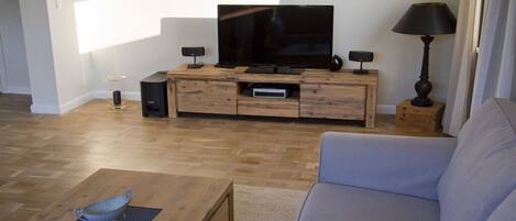 Una sala de estar moderna con un televisor de pantalla plana sobre un mueble de madera, un sofá gris y una mesa de centro con un cuenco decorativo.