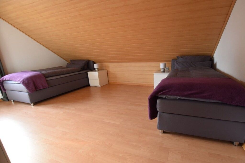 Een slaapkamer met twee bedden, een schuine houten balkenplafond en een witte nachtkastje.