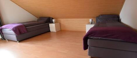 A bedroom with two beds, a wooden sloped ceiling, and a white nightstand.