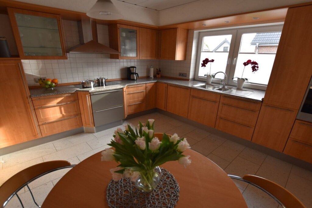A kitchen with wooden cabinets, a stainless steel sink, and a dining table with a vase of flowers.