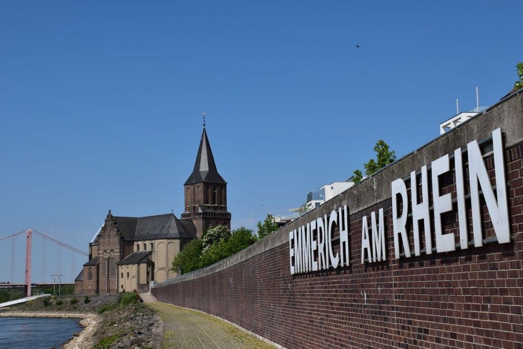 Um edifício histórico com uma placa de destaque exibindo 'EMMERICH AM RHEIN' e uma igreja com uma torre alta.