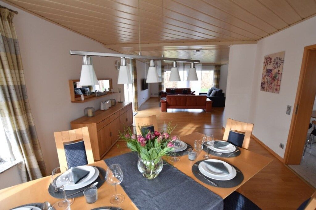 Un coin repas avec une table en bois dressée pour quatre personnes, un vase de fleurs et un luminaire suspendu.